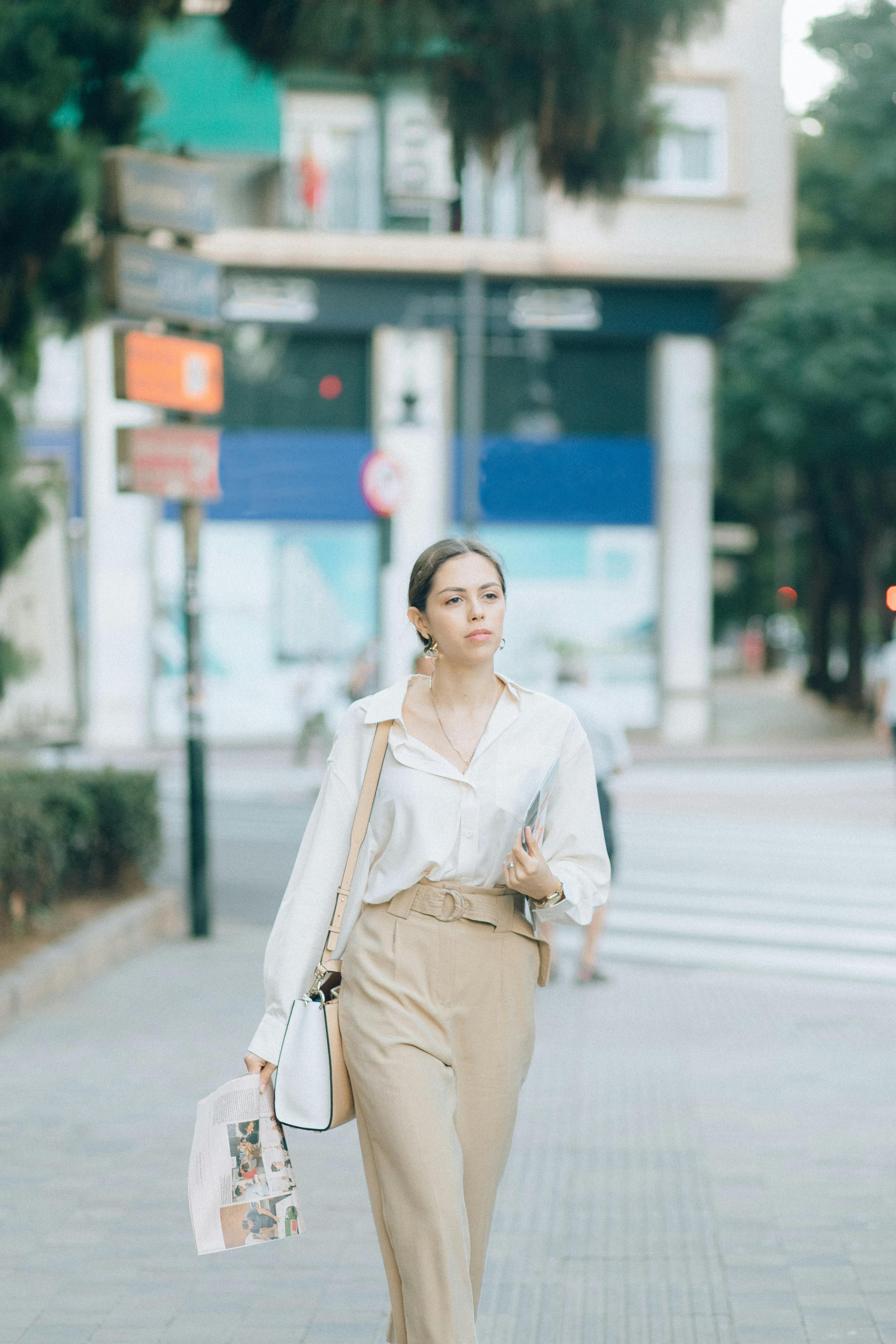 一位时尚女士自信地走在城市人行道上，穿着休闲别致的服装