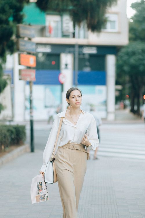 Free A fashionable woman walks confidently along a city sidewalk in casual chic attire. Stock Photo