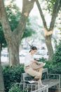 一位时尚的女士在绿树环绕的公园长凳上读着报纸