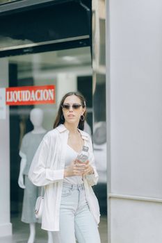 一位戴着太阳镜的时髦妇女在清算销售商店前拿着水瓶