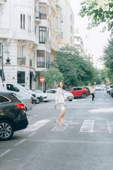 一位穿着时尚的女人正穿过城市街道的斑马线，背景是优雅的建筑