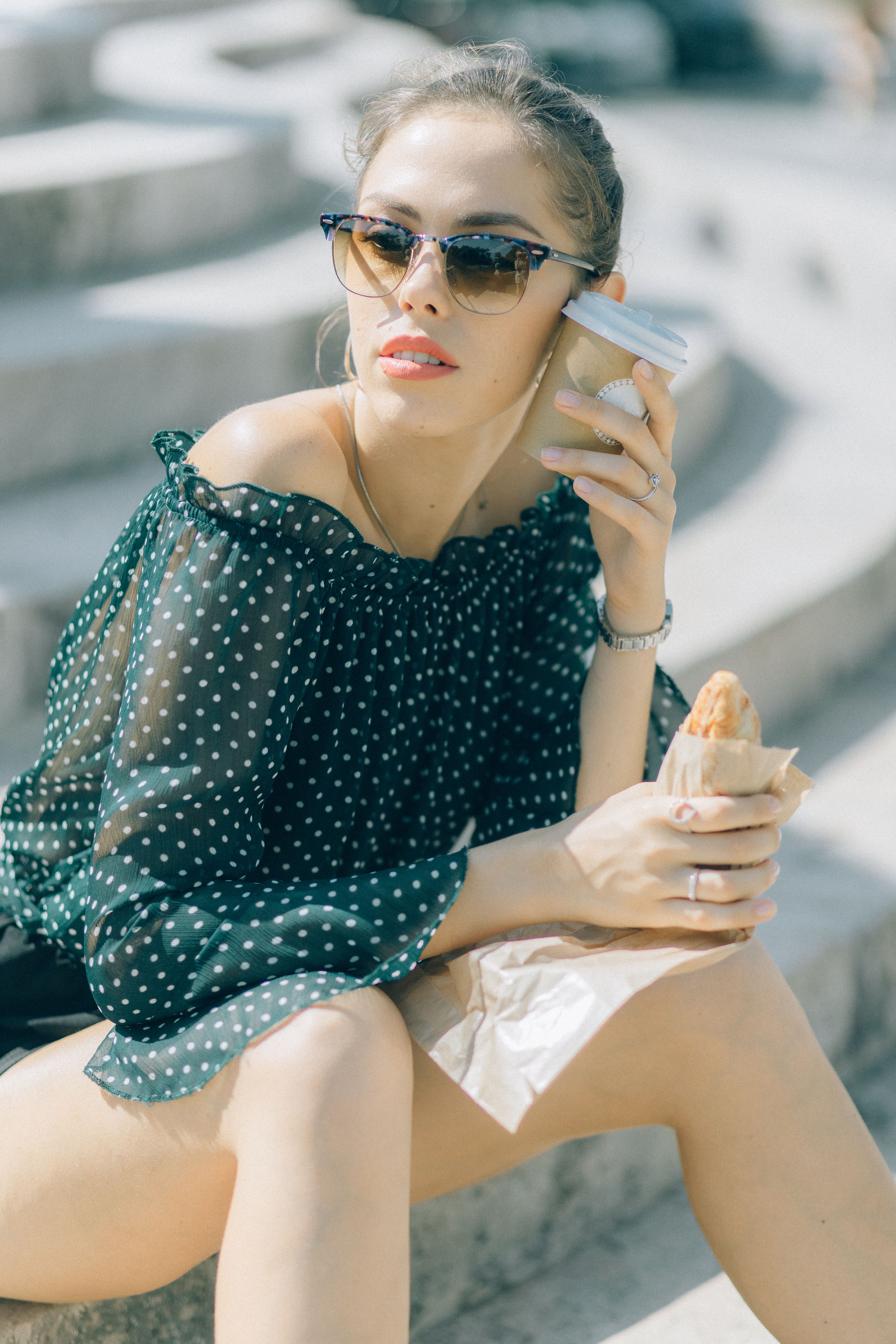 一位戴着太阳镜的时髦妇女，拿着咖啡和油酥点心，在楼梯上晒太阳