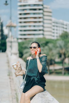 Smiling woman in off-shoulder blouse talking on phone outdoors during the day.