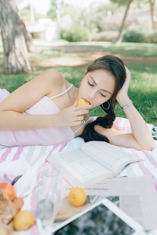 Free Woman Eating a Fruit While Reading Stock Photo