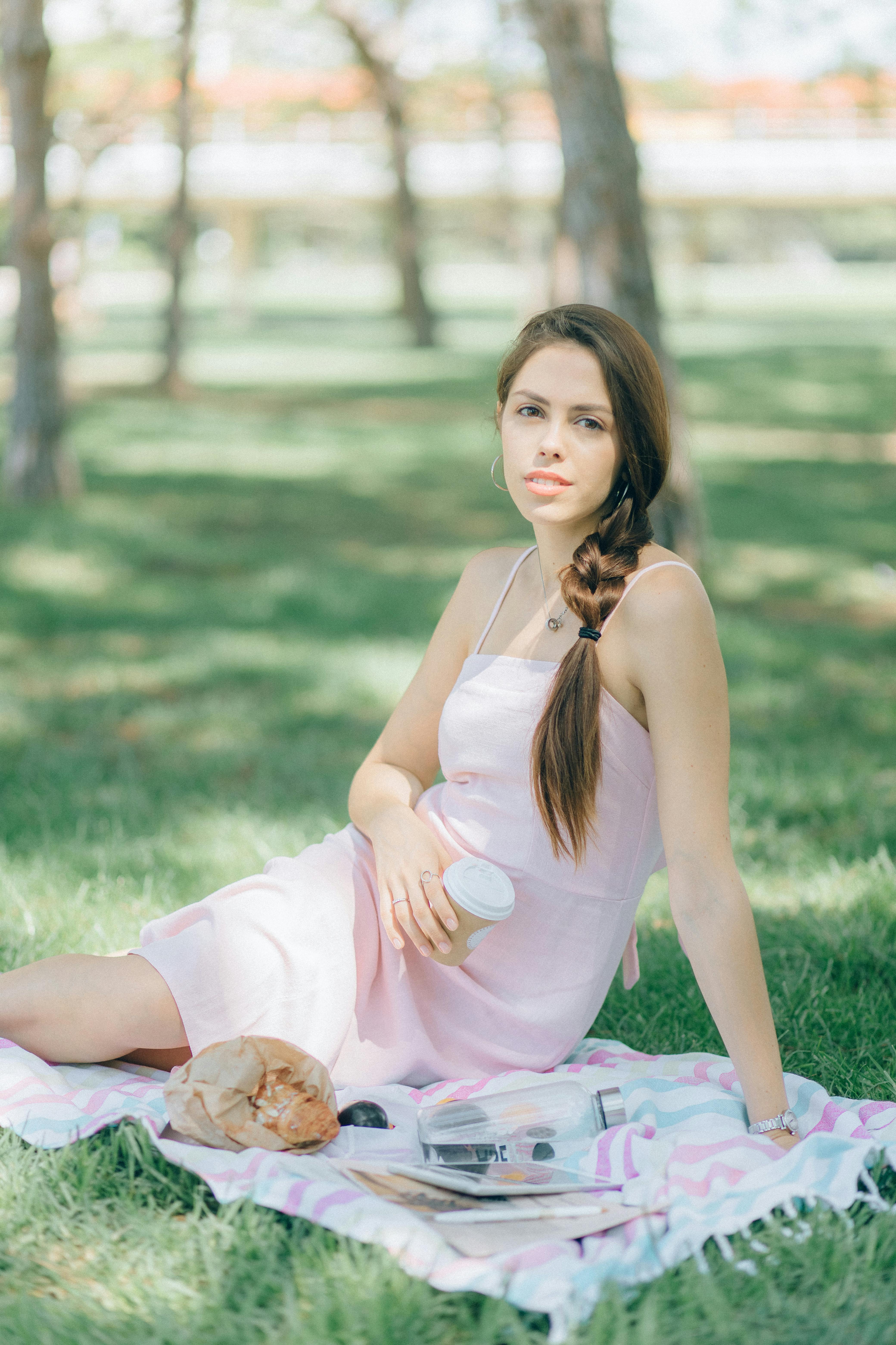 woman in white tank top and pink skirt sitting on green grass field carrying brown dog