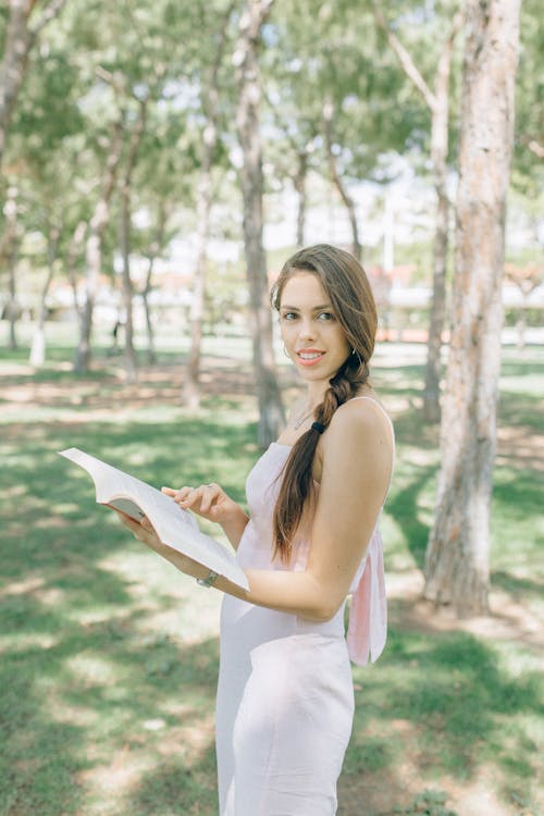 A Woman in a White Dress Reading a Book at a Park