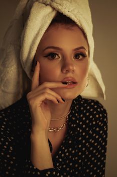 Young female with makeup in white towel on head and casual clothes touching face and looking at camera