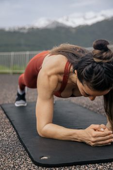 一位专注的女人正在以山脉为背景的瑜伽垫上做平板支撑