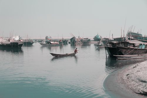 Free A tranquil scene of fishing boats docked at a harbor with a lone fisherman on the water. Stock Photo