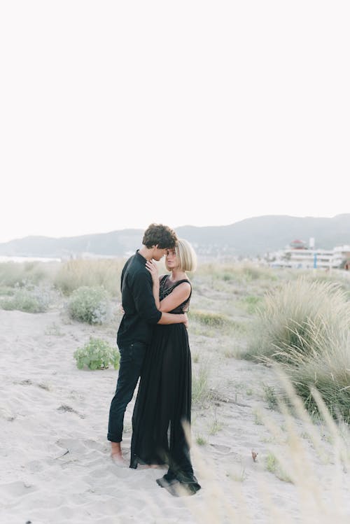 Couple in Black Clothing Embracing on Beach