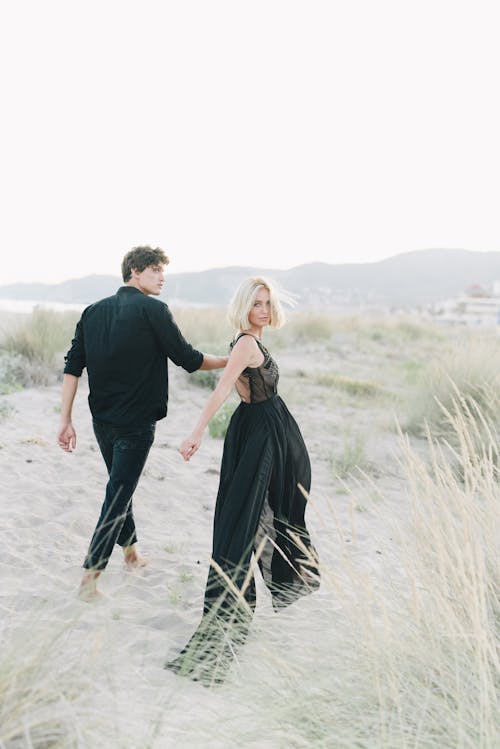 Free Man in Black Long Sleeves and Woman in Black Dress Holding Hands While Walking  Stock Photo