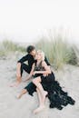 一对穿着黑色服装的情侣在长满高草的沙滩沙丘上拥抱