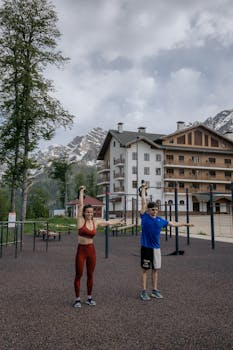 A man and woman lifting kettlebells in an outdoor gym by mountains