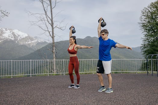 A fit couple exercises outdoors with kettlebells against a scenic mountain backdrop, showcasing a healthy lifestyle.