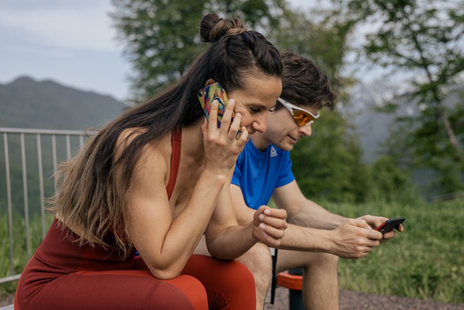 A couple in activewear using smartphones outdoors in a natural setting.