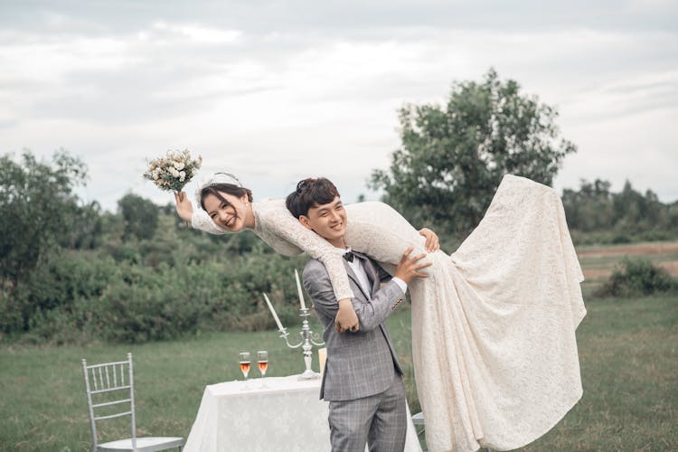 Happy Groom Carrying Bride Outdoors