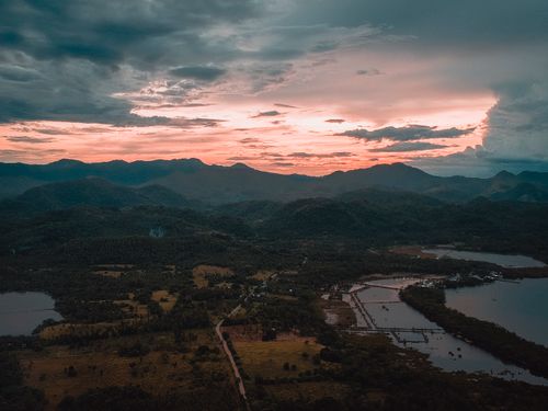 Free Aerial view of picturesque scenery of tropical green valley with trees and water plantations against mountains under colorful sky at sunset Stock Photo