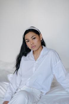 一位穿着白色服装的时尚年轻女子，平静地坐在室内的床上