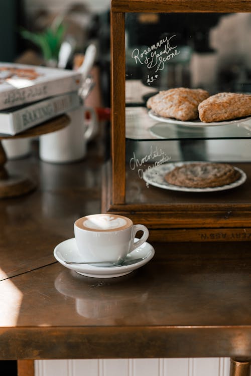 Free White ceramic cup with freshly brewed cappuccino on saucer placed on counter in modern cafeteria Stock Photo