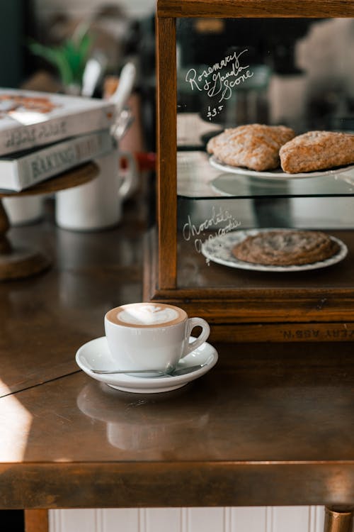 White ceramic cup with freshly brewed cappuccino on saucer placed on counter in modern cafeteria