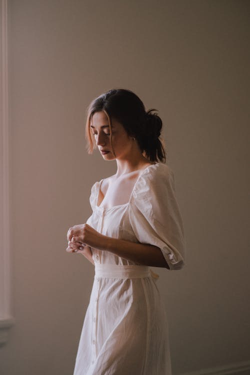 Dreamy young woman in white dress in light room