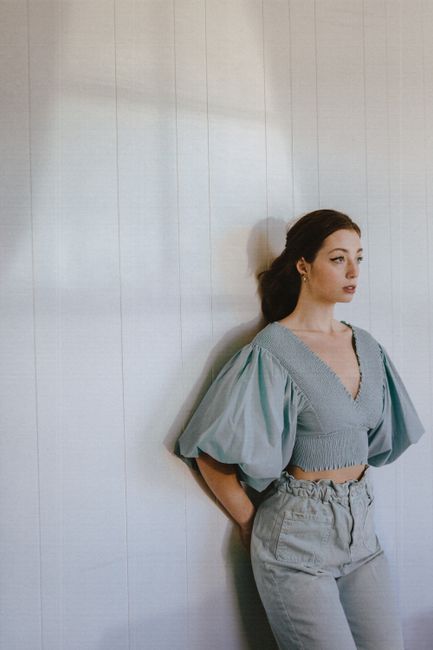 Young beautiful female wearing trendy outfit standing with hands behind back against white tiled wall and looking away calmly