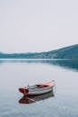 Scenery of small wooden boat moored on tranquil still pond surrounded by rough grassy hills under gray sky