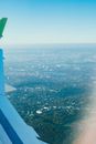 View of city with green vegetation and blue sky with horizon line from above through window of airplane flying in air