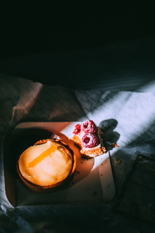Free From above of delicious cheesecake and cake topped with raspberry and powdered sugar served in box under sunbeam placed on bed in dark room Stock Photo
