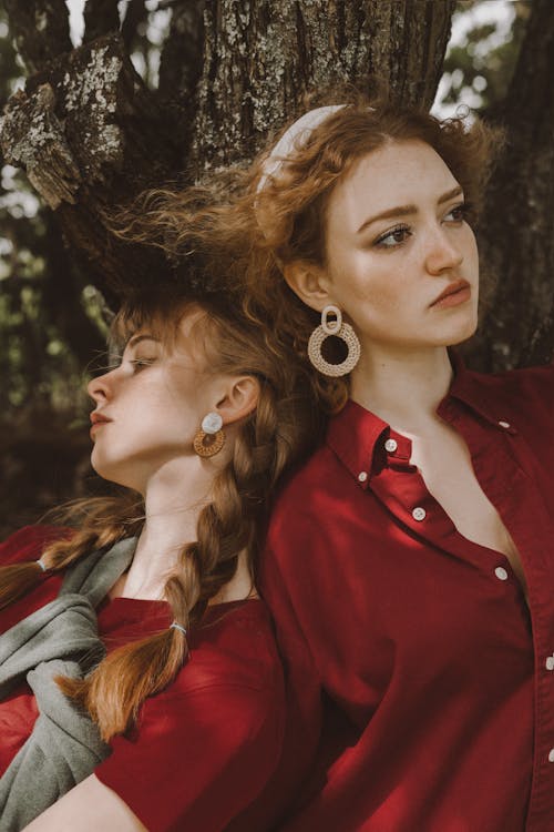 Stylish young women in bright red blouses near tree