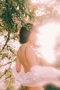 郁郁葱葱的树叶间，一个女人静立其中，阳光营造出梦幻般的宁静氛围