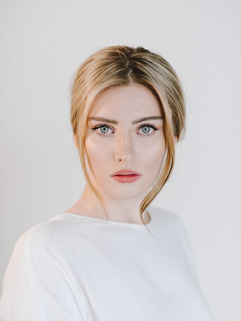 Young content tender female with eyeliner looking at camera on white background of studio