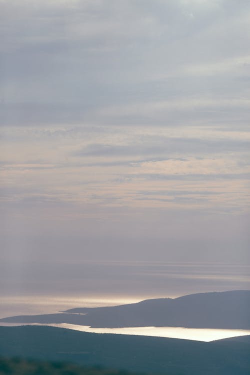 Free Breathtaking scenery of high hills surrounded with endless river under cloudy sky in evening Stock Photo