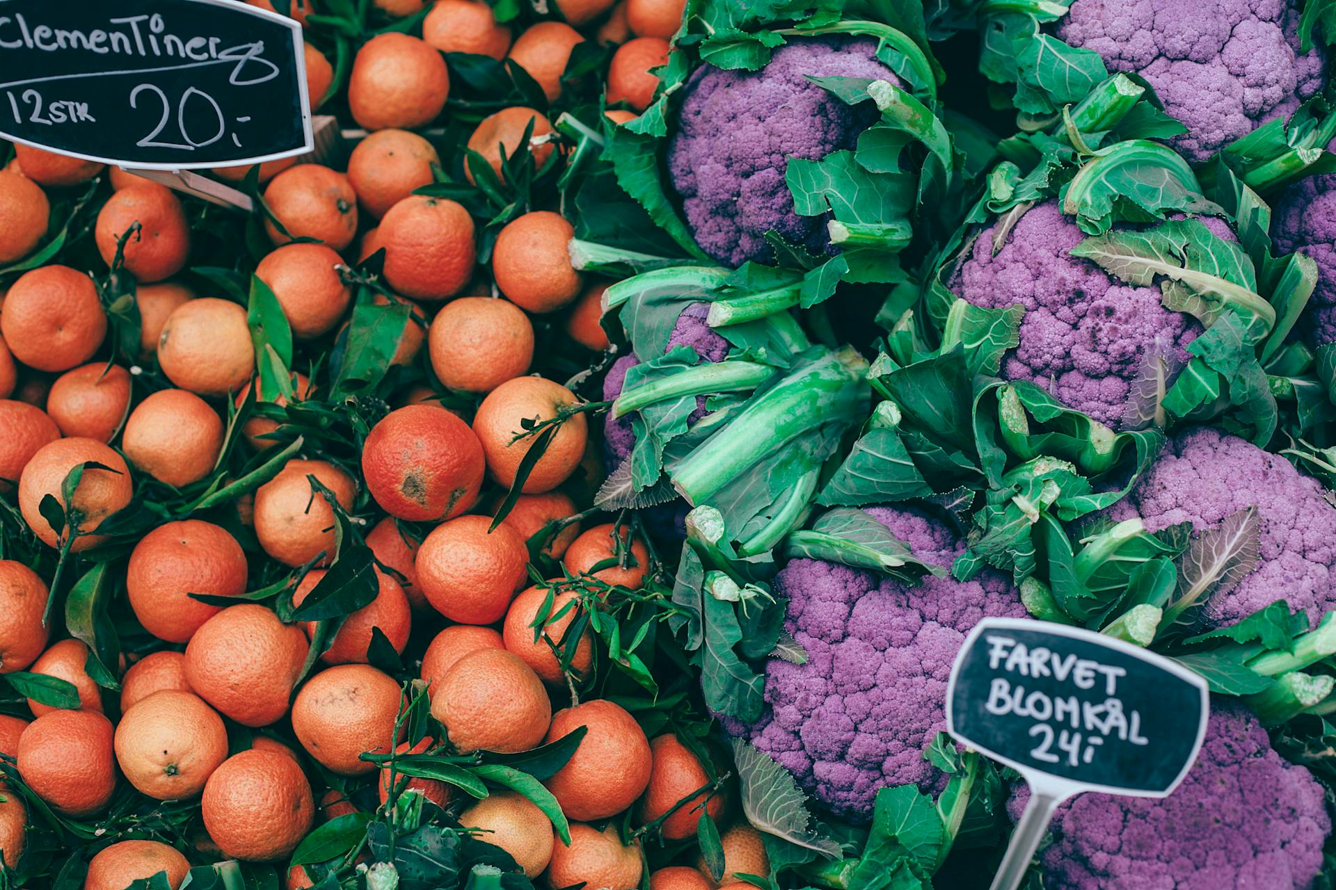 From above of fresh ripe colorful citrus fruits placed near violet healthy cauliflower on market