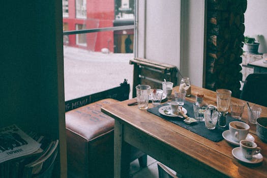 A wooden table in a cozy café with empty dishes and cups by the window.