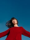 一名身穿红色连衣裙、闭着眼睛的女子沐浴在晴朗的蓝天下