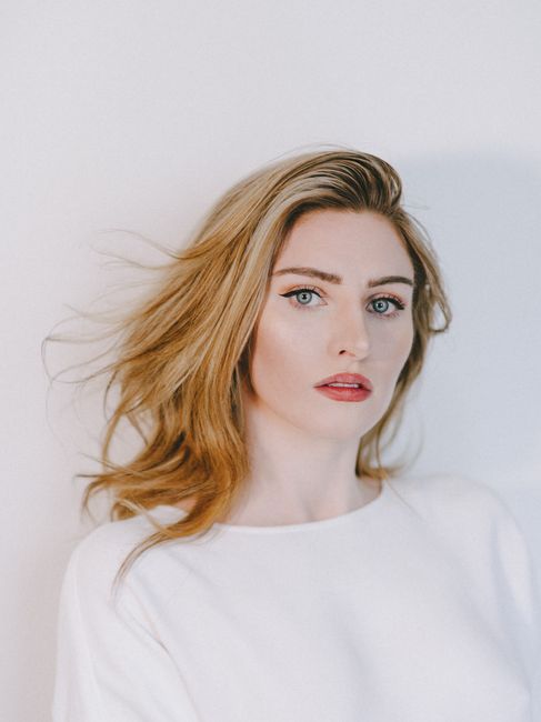 Attractive young female with long hair in white blouse on white background looking at camera