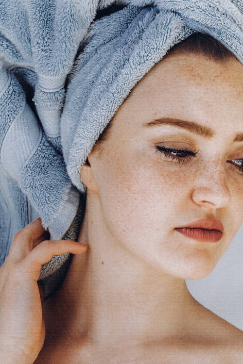 Portrait of pensive young beautiful female with freckles and towel on head after shower