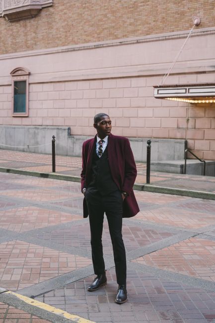 Full body of confident young African American male in stylish formal wear standing on paved walkway with hands in pockets and looking away