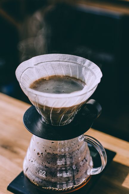 Fresh coffee pouring into glass jar from filter placed on wooden surface in daylight in cafe
