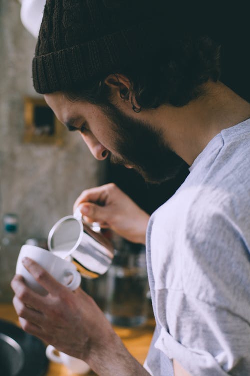 Faceless man pouring milk in coffee in cafe