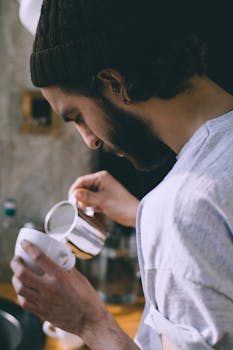Side view of a barista pouring milk into a cup of coffee indoors.