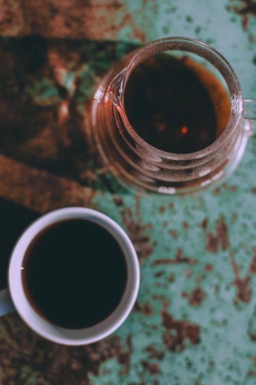 Free From above of white ceramic mug with coffee placed near glass decanter placed on shabby surface Stock Photo