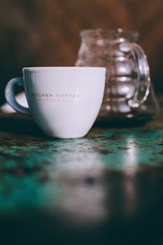 White ceramic cup with coffee near glass utensil placed on shabby surface in cafe