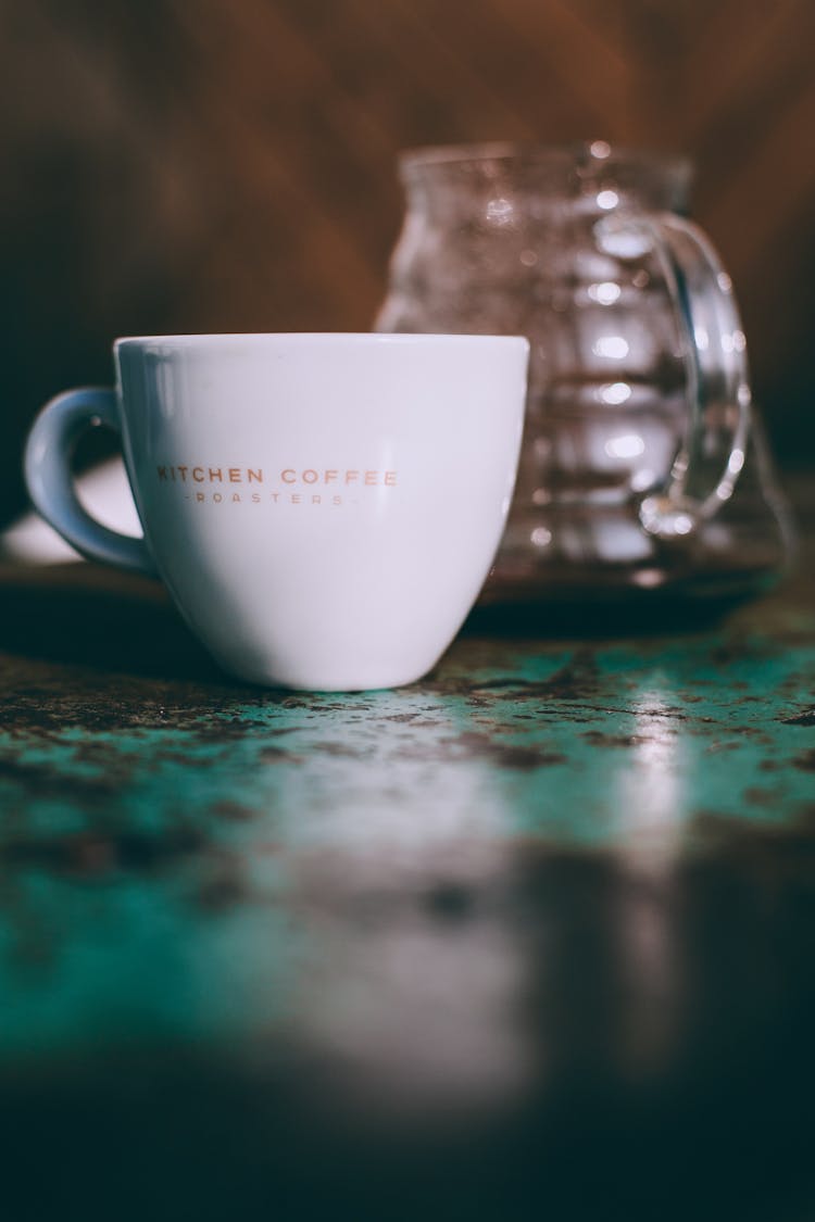 Mug With Coffee Near Brewing Pot On Table