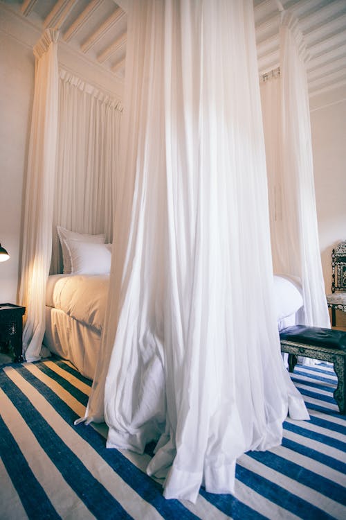 Spacious bedroom with large bed with white curtains hanging on ceiling in daylight