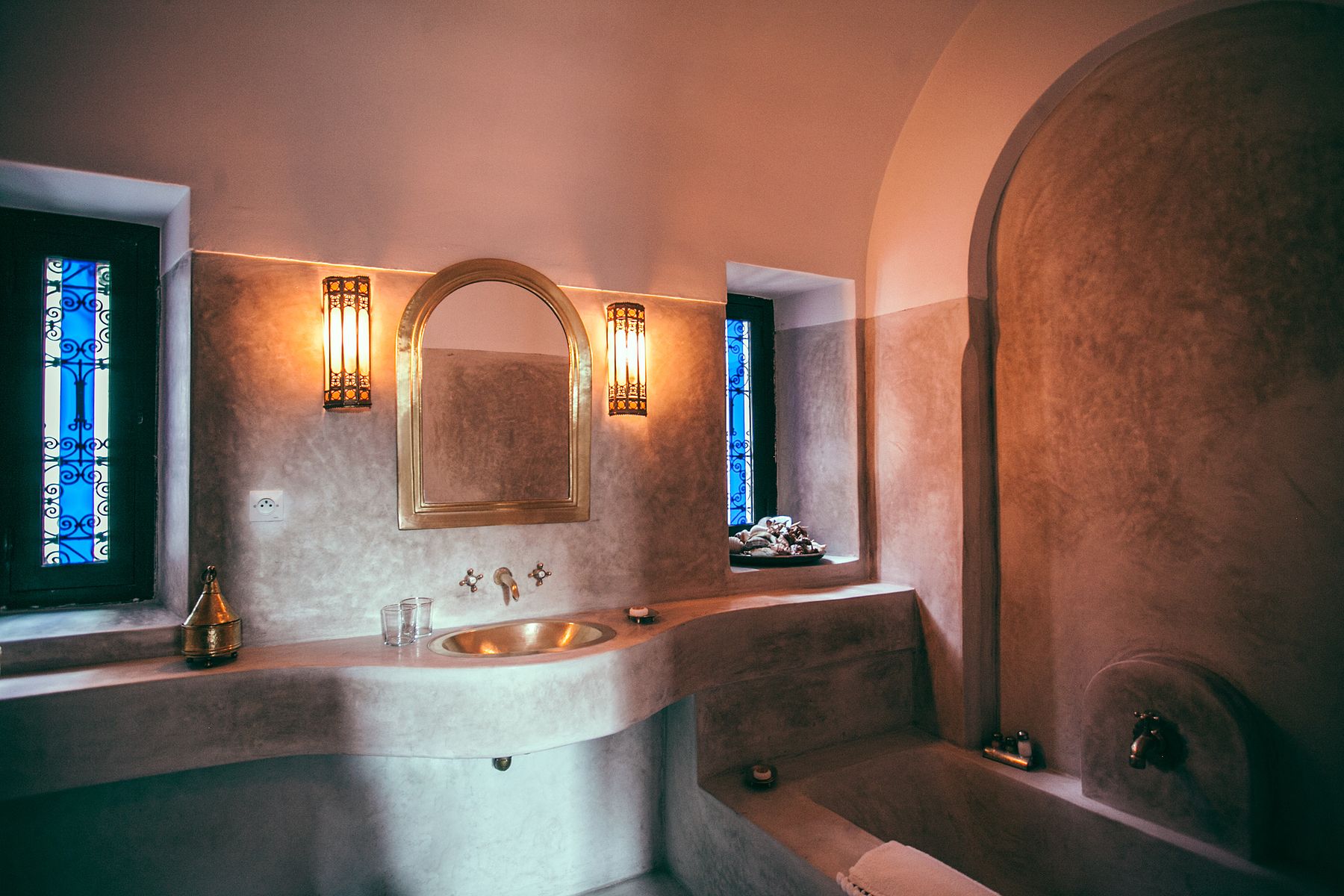Warm Mediterranean bathroom with curved plaster walls, an integrated basin, arched mirror, wall lanterns and a built-in bath