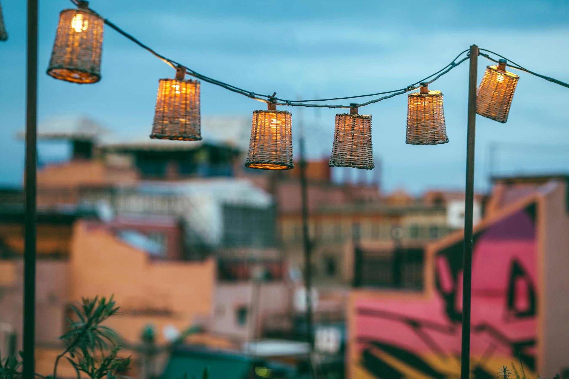 Set of handmade wicker lamps hanging on long rope between metal poles on roof