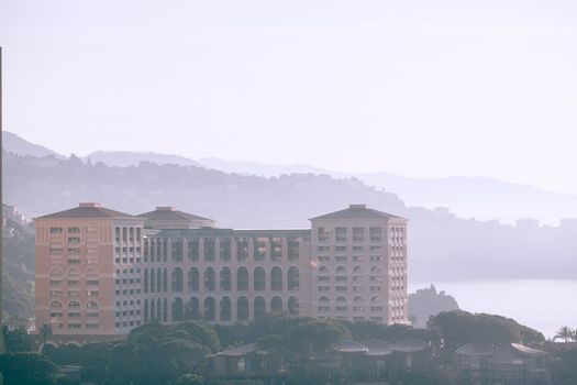Contemporary house located on bank of river near lush green trees against forest in mountainous area covered with fog