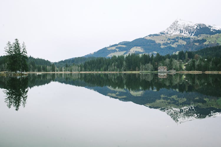 Calm Lake Reflecting Spectacular Mountain And Rural House